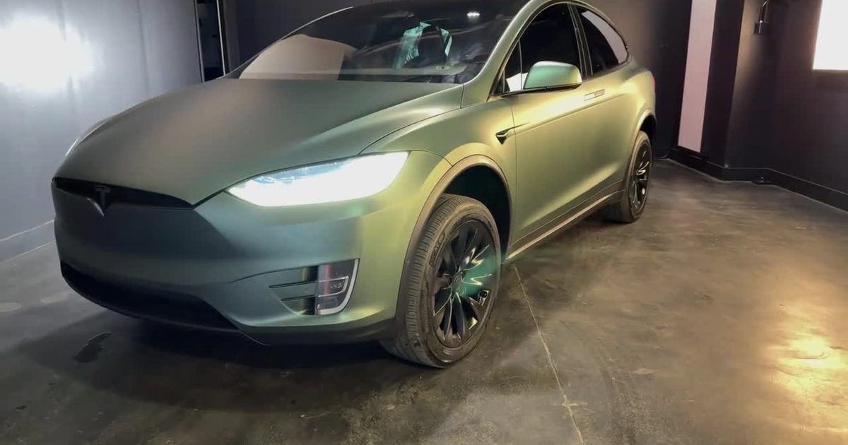 A matte green wrapped Tesla Model X with blacked-out trim, wheels and calipers in the Monaco Wheels shop