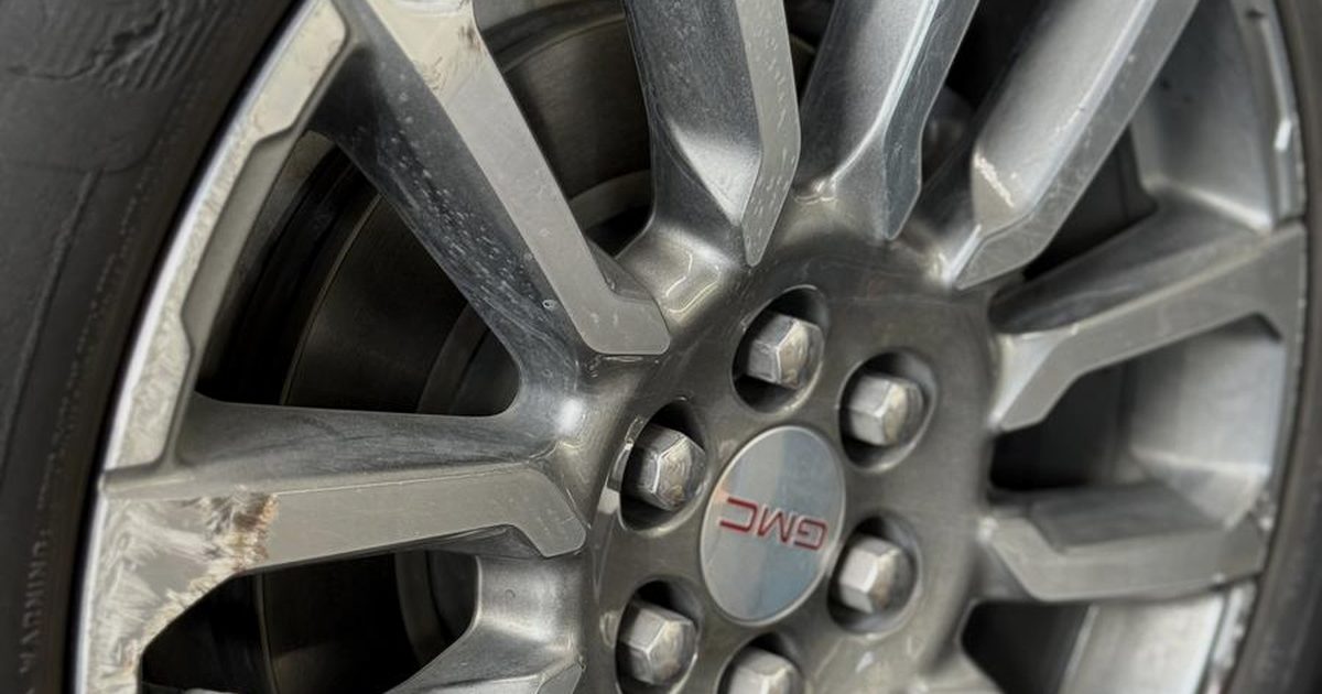 Close-up of curb rash along the lip and spokes of a GMC alloy wheel before repair